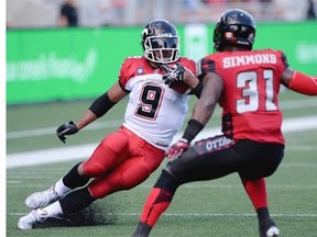 Calgary Stampeders' Jon Cornish, left, tries to avoid Ottawa Redblacks' Jasper Simmons during CFL action in Ottawa on Sunday, Aug. 24, 2014. THE CANADIAN PRESS/Sean Kilpatrick