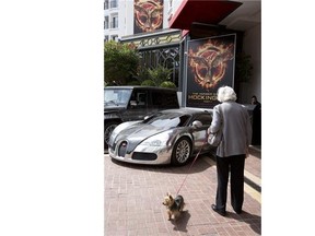 In this photo taken on Monday, May 12, 2014, a woman walking her dog looks at a Bugatti car and a poster for the “Hunger Games, Mockingjay: Part 1” at a hotel in Cannes, France. (AP Photo/Virginia Mayo)