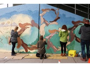 Four volunteers on their lunch break from jobs with the City of Calgary Waste Recycling Services along with artist Ryan Delve, left, and artist Mark Vazquez-MacKay, second from right, work on a mural on a concrete wall outside the Calgary Drop-In Centre on Thursday.