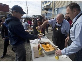 Yukon Premier Darrell Pasloski (right) and Northwest Territories Premier Bob McLeod serve a man a hamburger during Nunavut Day celebrations Wednesday July 9, 2014 in Iqaluit. Western premiers have been meeting in the community.