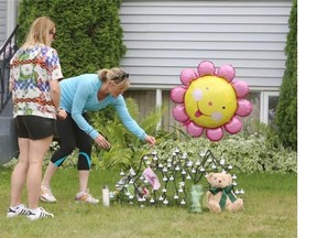 Natalie Stevenson and her mom place flowers and a balloon at the memorial to Alvin and Kathy Liknes and their five-year-old grandson, Nathan O’Brien, after police announced the missing-persons case is now being treated as a triple homicide.