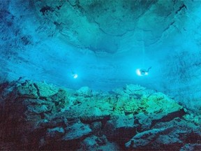 In this undated photo made available by Roberto Chavez Arce in May 2014, divers use lights to illuminate Hoyo Negro, an underwater cave in Mexico's Yucatan Peninsula where the remains of "Naia," a teenage girl who lived 12,000 to 13,000 years earlier, were found. Her skeleton and her DNA are helping scientists study the origins of the first Americans. An analysis of her remains was released Thursday, May 15, 2014 by the journal Science. Her DNA links her to an ancient land bridge connecting Asia and North America, and suggests she shares ancestors with the modern native peoples of the Americas. (AP Photo/Roberto Chavez Arce via Science)