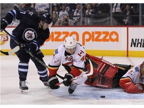 Calgarian Adam Lowry of the Winnipeg Jets battles for the puck with Flames defenceman Kris Russell in front of goaltender Jonas Hiller on Sunday.