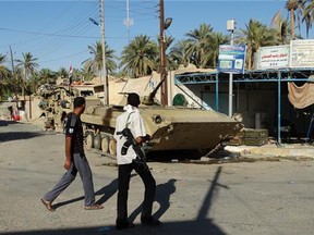 Men walk past an army tank on Sept. 10, 2014 in Barwanah, Iraq, after government forces retook the town from ISIS fighters.
