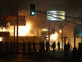 People gather around the burning stores Tuesday, Nov. 25, 2014, in Ferguson, Mo. A grand jury has decided not to indict Ferguson police officer Darren Wilson in the death of Michael Brown, the unarmed, black 18-year-old whose fatal shooting sparked sometimes violent protests.