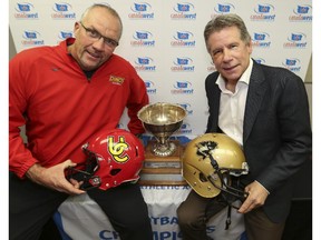 Blake Nill, Dinos' head coach, left, and Brian Dobie, Manitoba Bisons' head coach, pose for a photo with the Hardy Cup the day before their teams do battle at McMahon Stadium in Calgary, on November 14, 2014.