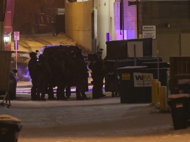 Members of the Calgary Police Service position themselves behind a dumpster in the alley behind the Bank of Montreal on 4th Street S.W.