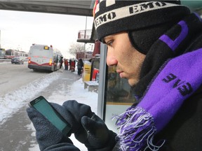 Binod Pokhrel checks his phone for the status on Route 23 as he waits at a bus stop along 36th Street N.E. on November 11, 2014.