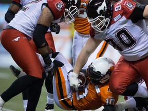 Calgary Stampeders' Juwan Simpson, left, and Quinn Smith, right, tackle B.C. Lions' Stefan Logan as he carries the ball during the second half of a CFL football game in Vancouver, B.C., on Friday November 7, 2014.