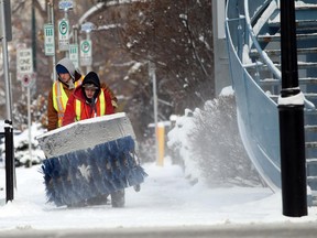 Thomas Resch pushes a large snowblower and Jacob Messom carries a shovel while cleaning sidewalks in Kensington on Monday, November 10, 2014. Calgary and southern Alberra has headed into very cold weather system on top of a storm that brought freezing rain and snow on November 10, 2014.