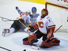 Calgary Flames' goalie Jonas Hiller, of Sweden, allows the winning goal to Vancouver Canucks' Chris Tanev, not seen, as Flames' Mark Giordano, left, checks Canucks' Daniel Sedin, of Sweden, during the overtime period of an NHL hockey game in Vancouver, B.C., on Saturday December 20, 2014.