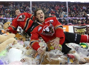 Calgary Hitmen's Kenton Helgesen (right) jumps into a pile of teddy bears during the annual Teddy Bear Toss game Sunday. Reader says Calgarians tossed more teddies than Edmontonians.