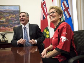 Ontario Premier Kathleen Wynne, right, wears a Calgary Stampeders jersey while meeting with Alberta Premier Jim Prentice at Queen's Park in Toronto, following a friendly bet on the Grey Cup.