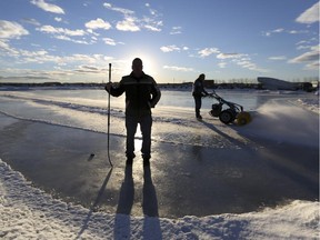 Norm Price is silhouetted on his 5-acre skating rink just east of Stony Trail while a volunteer, Billy Ritcher, clears snow off the ice, in Calgary, on January 20, 2015.