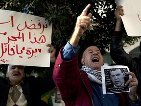 A Palestinian protester carries a banner that reads in Arabic "we refuse to receive this criminal, get out you child killer," while another protester chants slogans and holds a photo of Canadian Foreign Minister John Baird during Baird's meeting with Palestinian Foreign Minister Riad Malki.