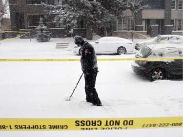 A Calgary Police investigator uses a metal detector to sweep the area in front of the house where 6 people were shot early New Years morning. Police still had the 1900 block of 36th Street SW closed off as they investigated in heavy snow Friday January 2, 2015.