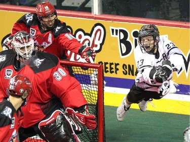 Calgary Roughnecks defenceman Mike Carnegie, background, tried to stop a flying Edmonton Rush transition Jarrett Davis as he stuffed the ball into the net of Roughnecks goalie Mike Poulin during NLL game action at the Scotiabank Saddledome on January 24, 2015.