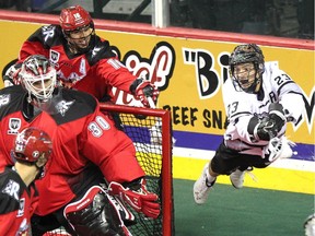 Calgary Roughnecks defenceman Mike Carnegie, background, tries to stop a flying Edmonton Rush transition Jarrett Davis as he stuffs the ball into the net of Roughnecks goalie Mike Poulin during Saturday's game.