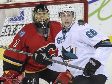 Calgary Flames goalie Jonas Hiller, and San Jose Sharks Melker Karlsson watch a flying puck in front of a crowded net during third period action at the Saddledome in Calgary, on February 4, 2015. The Flames came out on top 3-1.