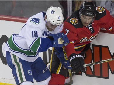 Calgary Flames' TJ Brodie battle Vancouver Canucks Ryan Stanton in the boards during game action at the Saddledome in Calgary, on February 14, 2015.