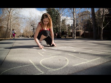 Melissa Paquette chalks the date of an upcoming protest against proposed antiterrorism bill C-51 along the Prince's Island pathway in Calgary on Friday, March 27, 2015.