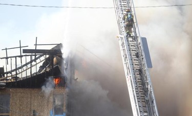 A firefighters climbs a ladder as fire below engulfs a building under construction at 17th Avenue South and Centre Street Saturday afternoon March 7, 2015.