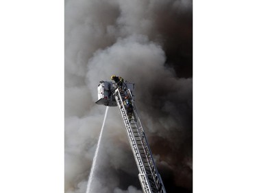 Two firefighters climb a ladder as fire below engulfs a building under construction at 17th Avenue South and Centre Street Saturday afternoon March 7, 2015.
