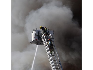 Two firefighters climb a ladder as fire below engulfs a building under construction at 17th Avenue South and Centre Street Saturday afternoon March 7, 2015.