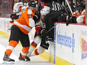 Carlo Colaiacovo of the Philadelphia Flyers crunches Josh Jooris  of the Calgary Flames as linesmen Scott Driscoll goes over the boards in the first period at Wells Fargo Center on Tuesday in Philadelphia. The Flames are still working as hard as they can to make the playoffs, even without captain Mark Giordano.