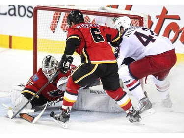 Calgary Flames goalie Karrie Ramo kept his eye on the puck as it deflected off the skate of defenceman Dennis Wideman while Columbus Blue Jackets centre Artem Anisimov looked to tip it in during second period NHL action at the Scotiabank Saddledome on March 21, 2015.