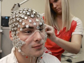 In this May 31, 2013, photo research assistant Sara Mason places an EEG net for detecting brain activity on fellow assistant Kevin Real, at the University of Nebraska's Center for Brain, Biology and Behavior in Lincoln, Neb. The center was working on a project that would allow football players who took a hit to the head to slip on the electrode-covered mesh cap and have medical staff analyze the player's brain waves on the spot and determine within 10 minutes whether he can safely return to the game or whether he has sustained a concussion and, if so, how severe. Health providers have yet to settle on exactly what to do to prevent and treat concussions.