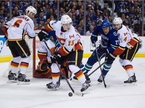 Calgary Flames' Johnny Gaudreau (13) moves the puck as Dennis Wideman (6) watches and Kris Russell (4) checks Vancouver Canucks' Shawn Matthias (27) during the first period of game 2 of an NHL Western Conference first round playoff hockey series in Vancouver, B.C., on Friday April 17, 2015.