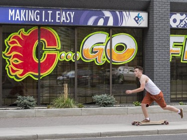 A long boarder zips by as Garry Peck, of Sasquatch Art and Display, puts the finishing touches on a "Go Flames!" window painting on 8th St. S.W. in Calgary, on April 29, 2015.