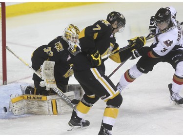 Calgary Hitmen's Kenton Helgesen tries to slap one passed the Brandon Wheat Kings' Eric Roy and goalie Jordan Papirny during WHL playoff action at the Saddledome in Calgary, on April 29, 2015.