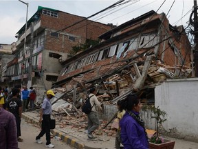 Nepalese people walk past a collapsed bullding in Kathmandu after an earthquake on April 25, 2015. A massive 7.8 magnitude earthquake killed hundreds of people April 25 as it ripped through large parts of Nepal, toppling office blocks and towers in Kathmandu and triggering a deadly avalanche that hit Everest base camp.