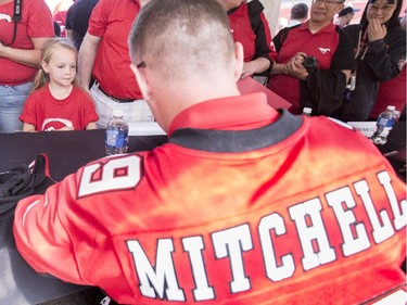 A young fan watches as Calgary Stampeders quarterback Bo-Levi Mitchell signs her jersey at the annual Stampeders Fanfest at McMahon Stadium in Calgary, on May 23, 2015.