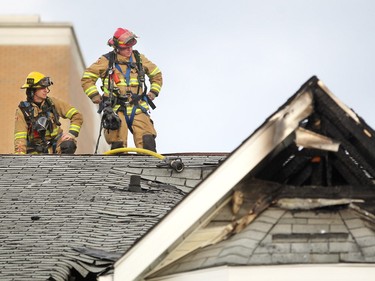 Firefighters sit on the peak of the roof as they work to extinguish hot spots following a two-alarm fire at a four-storey condo building in the 2200 block of 1st Street S.W.