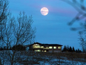 The full moon rises as the sunset lights up windows on an acreage in Springbank on Thursday February 13, 2014.