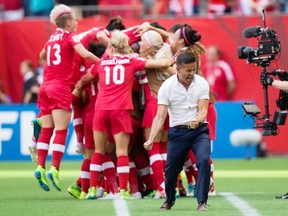 Canada coach John Herdman, right, celebrates as Josee Belanger, back, is mobbed by her teammates after scoring against Switzerland.