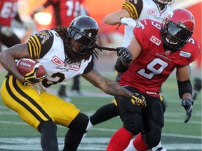 Calgary Stampeders Jon Cornish gives a tug on the Hamilton Tiger-Cats Johnny Sears Jr. during their season opener at McMahon Stadium, on June 26, 2015.