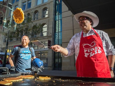 Calgary Herald reporter Trevor Howell, left, watches as Mayor Naheed Nenshi flips pancakes at Calgary Economic Development's sixth annual First Flip on Stephen Avenue in Calgary on Thursday.