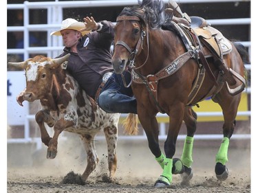 Dustin Walker shows the rodeo crowd how it's done for a first place finish during Day 9 of steer wrestling rodeo action at the 2015 Calgary Stampede,, on July 11, 2015.