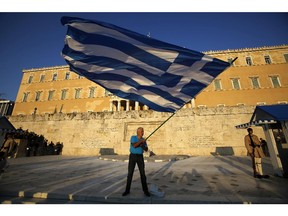 A pro-Euro demonstrator waves a Greek flag in front of the Greek Parliament as riot police, left, block an entrance of a building during a rally in Athens on July 9, 2015. Greece's government is racing to finalize a plan of reforms for its third bailout, hoping this time the proposal will meet with approval from its European partners and stave off a potentially catastrophic exit from Europe's joint currency, the euro, within days.