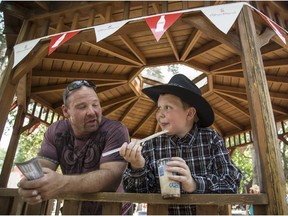 Dave Chouinard and his son Gabriel enjoy a slush drink under the gazebo in Weadickville to beat the summer heat at the Calgary Stampede in Calgary on Thursday, July 9, 2015.