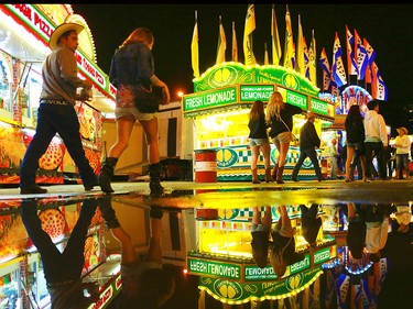 Stampede goers are reflected in a puddle left over from the afternoon's hail storm as the midway slowly winds down near midnight on July 4, 2015.