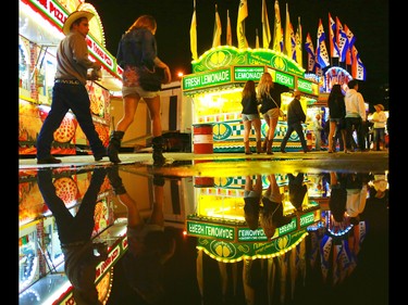 Stampede goers are reflected in a puddle left over from the afternoon's hail storm as the midway slowly winds down near midnight on July 4, 2015.