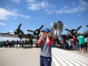 Ming Chen, 10, plugs his ears as a CF-18 flies overhead on the main runway with a WW II b-17 bomber Sentimental Journey in the background during the Wings Over Springbank air show at Springbank Airport west of Calgary on July 19, 2015.
