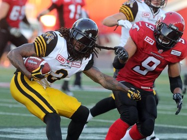 Calgary Stampeders Jon Cornish gives a tug on the Hamilton Tiger-Cats Johnny Sears Jr. during their season opener at McMahon Stadium, on June 26, 2015.