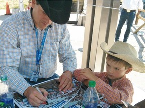 Chuckwagon driver Doug Irvine gets some help from six-year-old son Britton in signing autographs on Thursday at the Calgary Stampede.