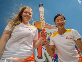 Haley Irwin, left, and Carol Huynh pose with a Pan Am games torch on their stampede float at Riverfront Avenue in Calgary on Thursday.